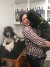 a woman is hugging two poodles in a salon