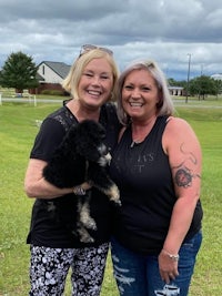 two women standing next to each other holding a black dog