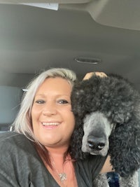 a woman holding a black poodle in the back seat of a car